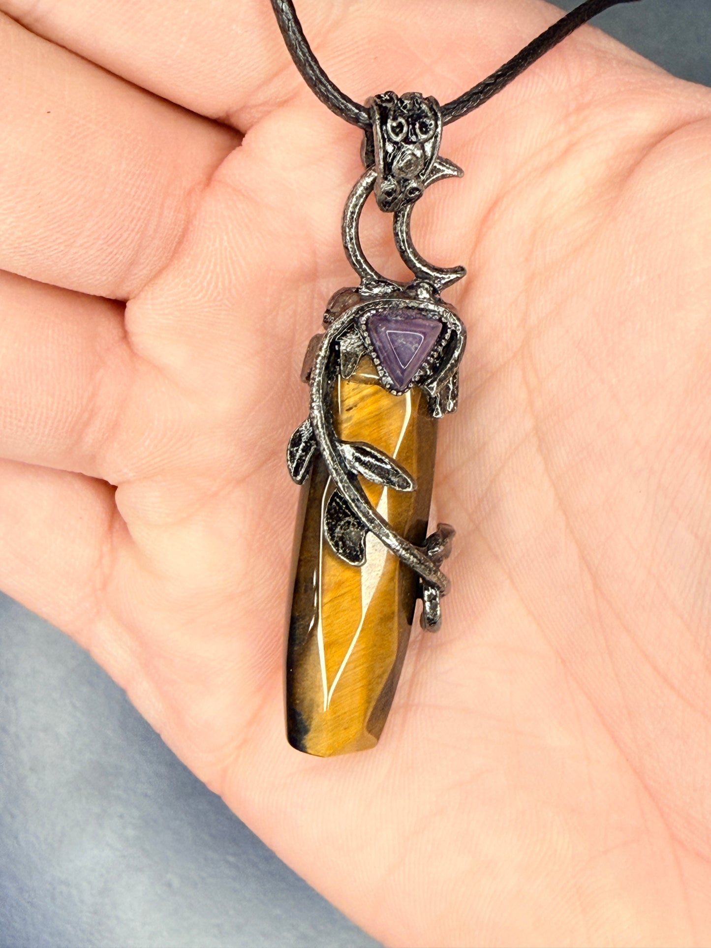 Hand holding an intricate tiger's eye pendant with leaves wrapping around it