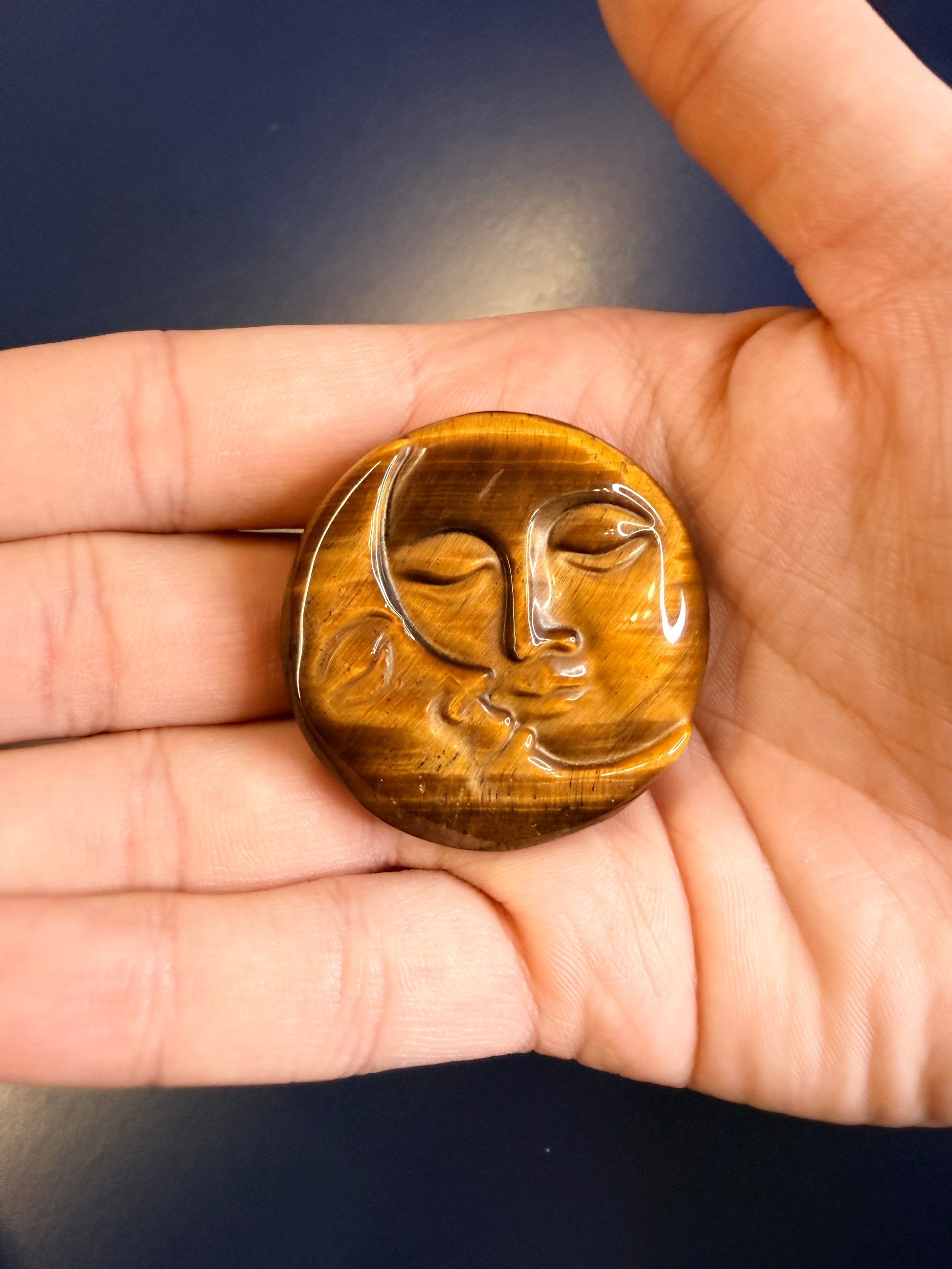 Hand holding a gold colored sun and moon face crystal on a blue background