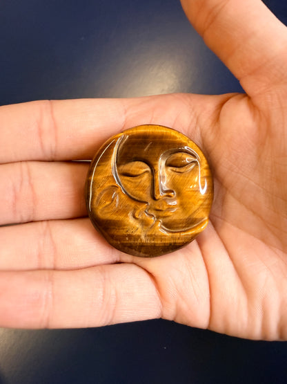 Hand holding a gold colored sun and moon face crystal on a blue background
