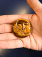 Hand holding a gold colored sun and moon face crystal on a blue background