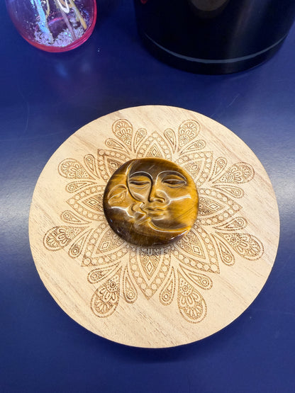 A gold colored sun and moon face crystal on a decorative wooden coaster on a blue background