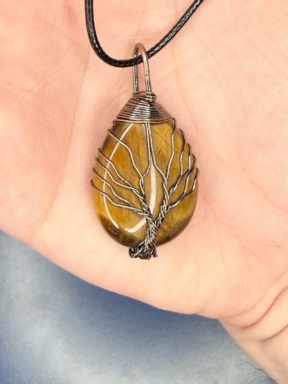 Hand holding a tiger's eye tree of life wire wrap pendant