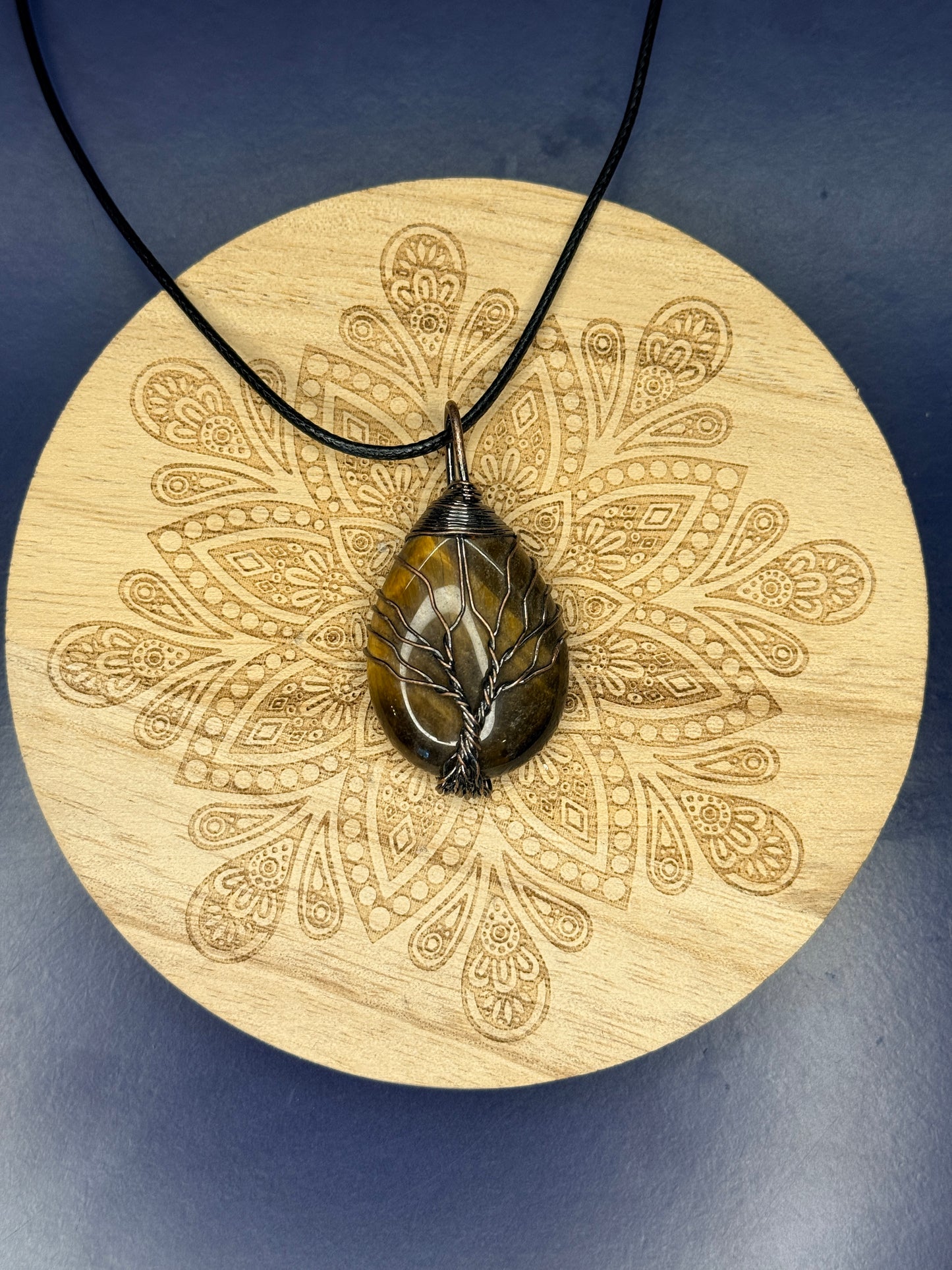 Tiger's eye tree of life pendant on a decorative wooden coaster against a blue background
