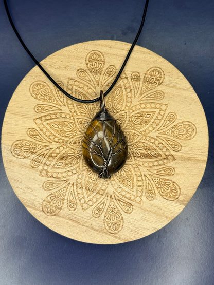 Tiger's eye tree of life pendant on a decorative wooden coaster against a blue background