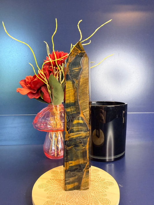 Gold and black tiger's eye tower on a wooden coaster in front of a red flower in a vase and black jar