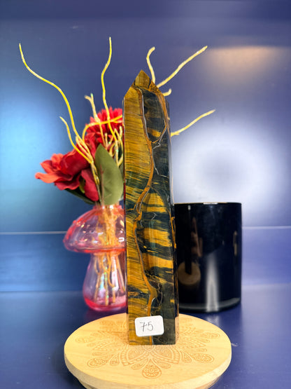 Gold and black tiger's eye tower on a wooden coaster in front of a red flower in a vase and black jar