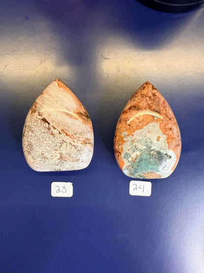Two red, white, and magenta unicorn jasper freeforms on a blue background