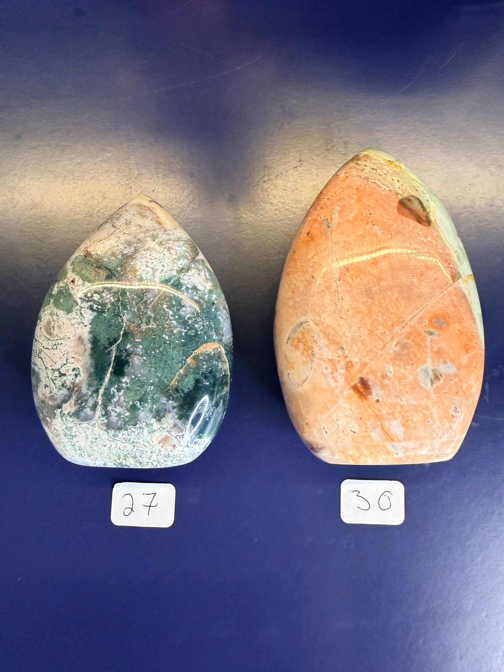 Two white, green, and peach unicorn jasper freeforms on a blue background