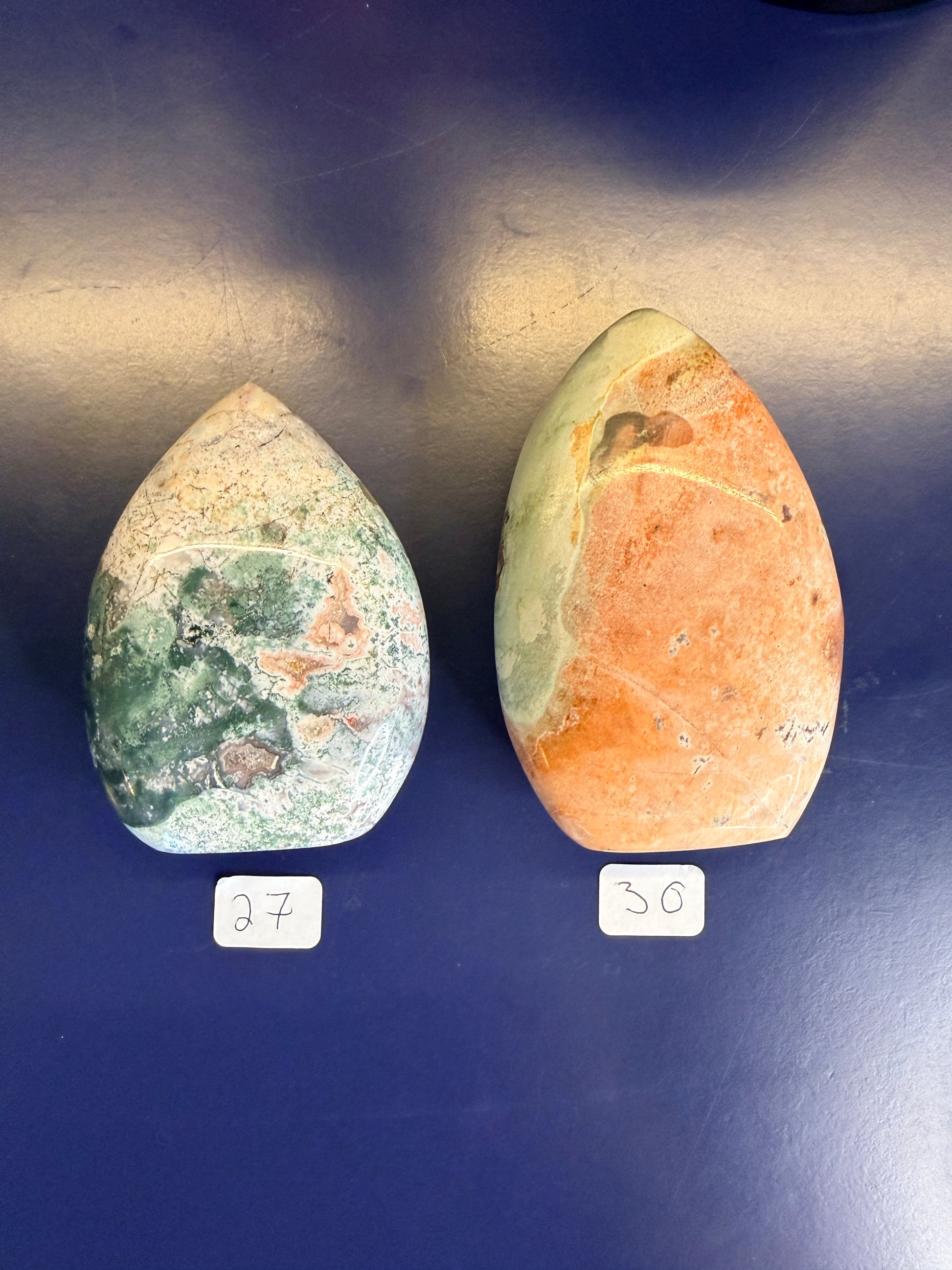 Two white, green, and peach unicorn jasper freeforms on a blue background