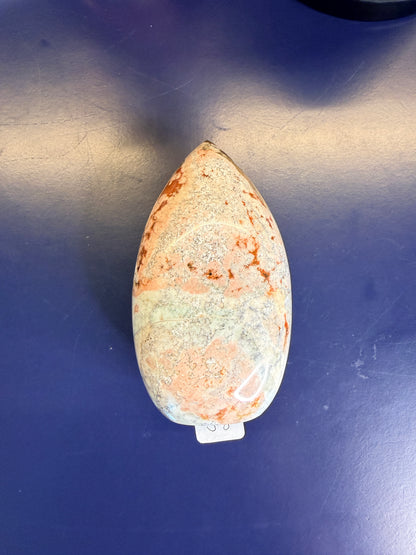  A green, white, and peach unicorn jasper free form on a blue background