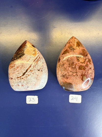 Two red, white, and magenta unicorn jasper freeforms on a blue background