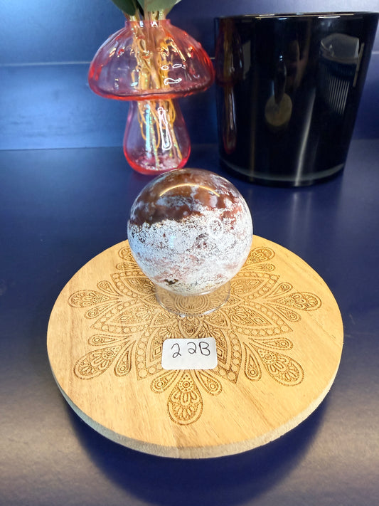 White and magenta unicorn jasper sphere on a decorative wooden coaster in front of a mushroom vase and black jar