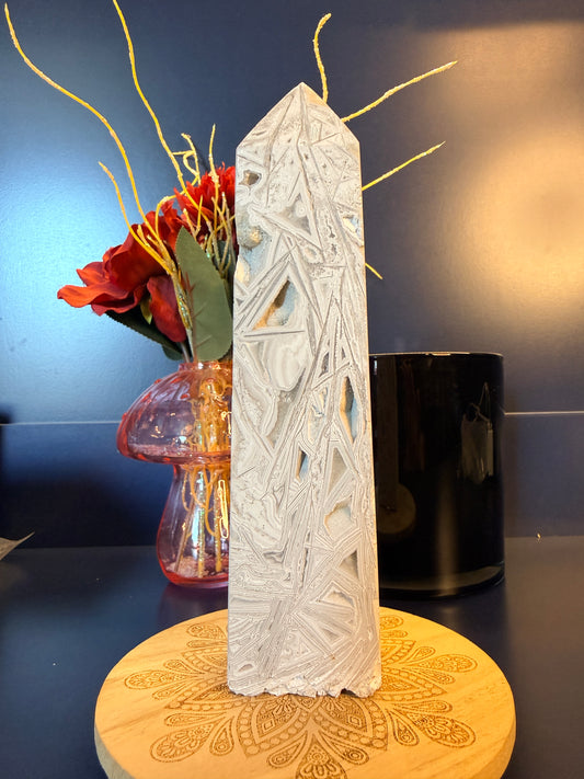 A large, intricate crystal tower sitting on a decorative wooden coaster in front of a glass mushroom and black jar