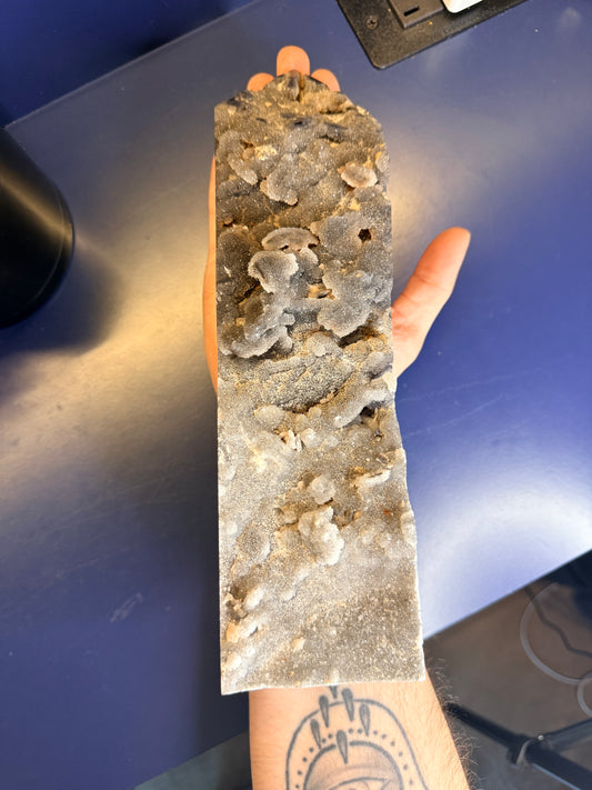 Hand holding a large grey sparkly sphalerite tower that rests on the forearm against a blue background