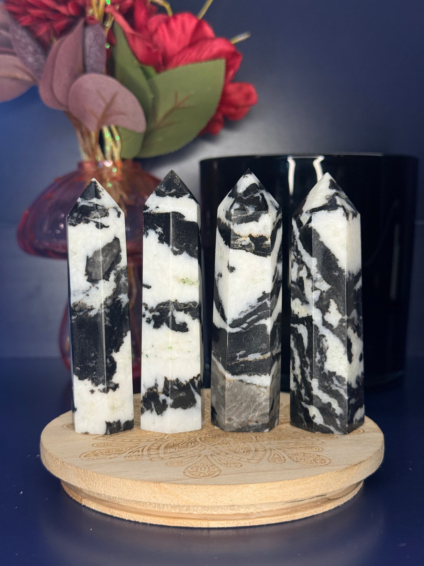 Four black and white zebra jasper towers in front of a pink vase and black jar on a wooden coaster against a blue background