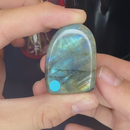 Hands holding multiple labradorite freeforms showing their blue flash in front of a mushroom vase and black jar